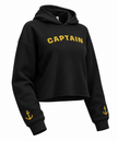 A black cropped hoodie sweatshirt with 'CAPTAIN' printed in yellow arched letters across the chest and a small yellow anchor graphic on each sleeve cuff, shown on a plain white background.